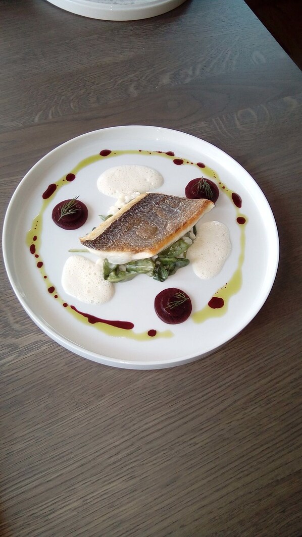 A white plate with a fish, greens, and white sauce, with red sauce and olive oil drizzles. - Ratskeller Wiedenbrück (Rheda-Wiedenbruck)