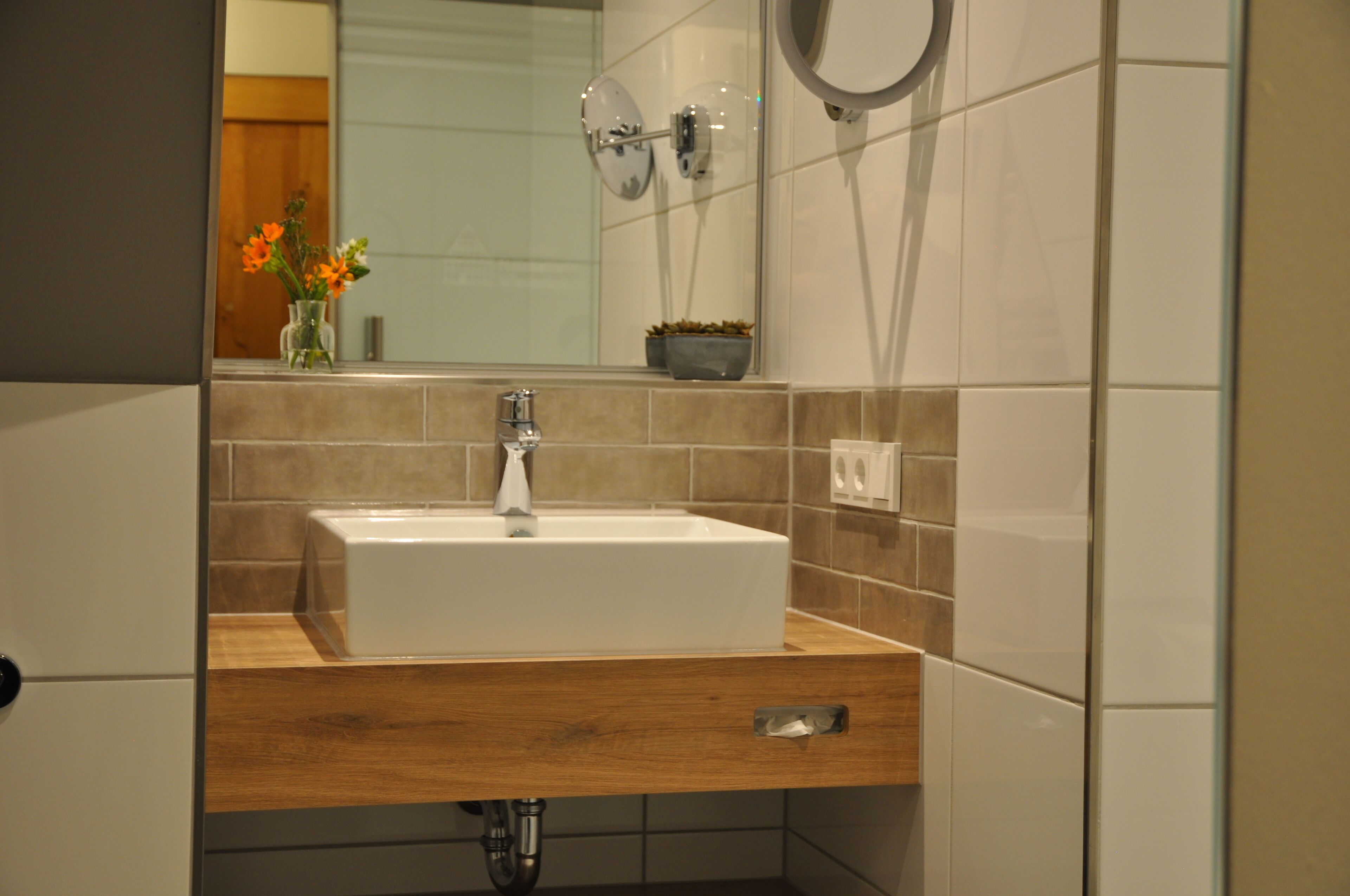 Un baño con lavamanos blanco, encimera de madera y azulejos color beige.