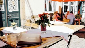 An outdoor dining area with wooden tables, a vase with red flowers, and a menu stand. - Ratskeller Wiedenbrück (Rheda-Wiedenbruck)