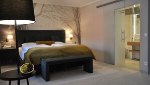 A modern bedroom with a large bed, bedside lamps, a bench, and a bowl of fruit on a small table. - Ratskeller Wiedenbrück (Rheda-Wiedenbruck)