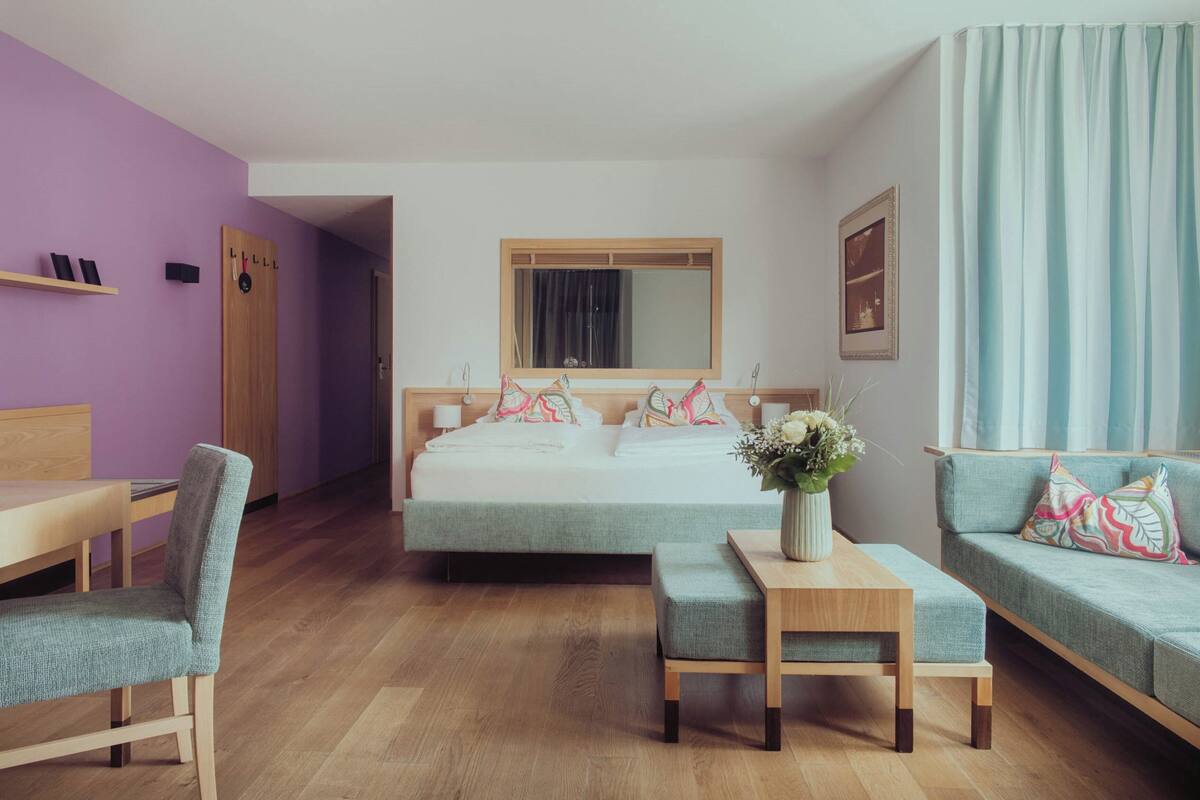 Un dormitorio con una cama, un escritorio, una silla, un sofá y una mesita con un jarrón de flores.