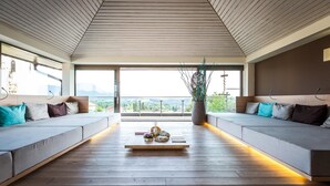 A modern living room with a wooden floor, two sofas with cushions, a coffee table with decorative items, and a view of the city through large windows.
