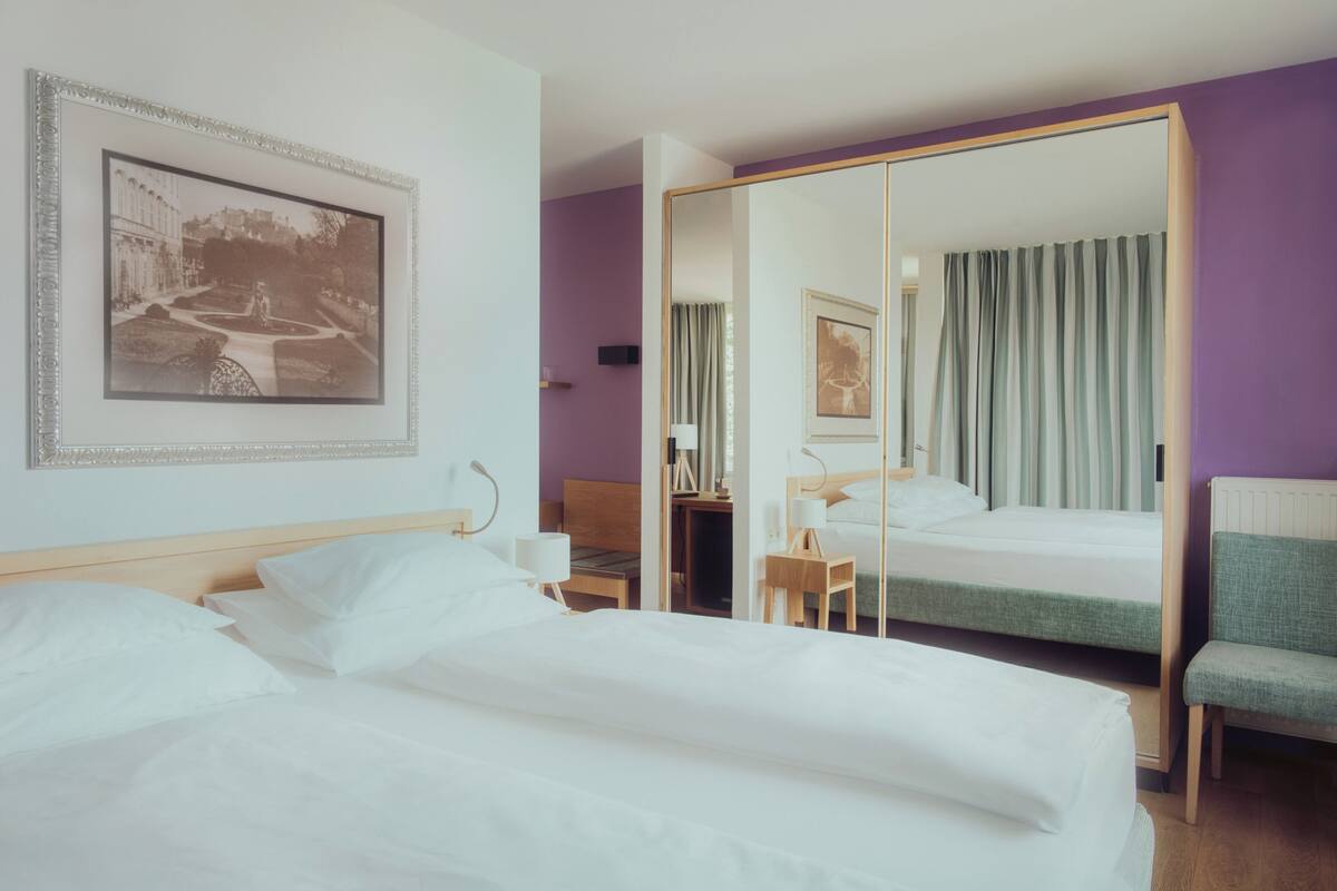 Habitación de hotel con una cama grande, un escritorio, una silla, un espejo y un cuadro en la pared.