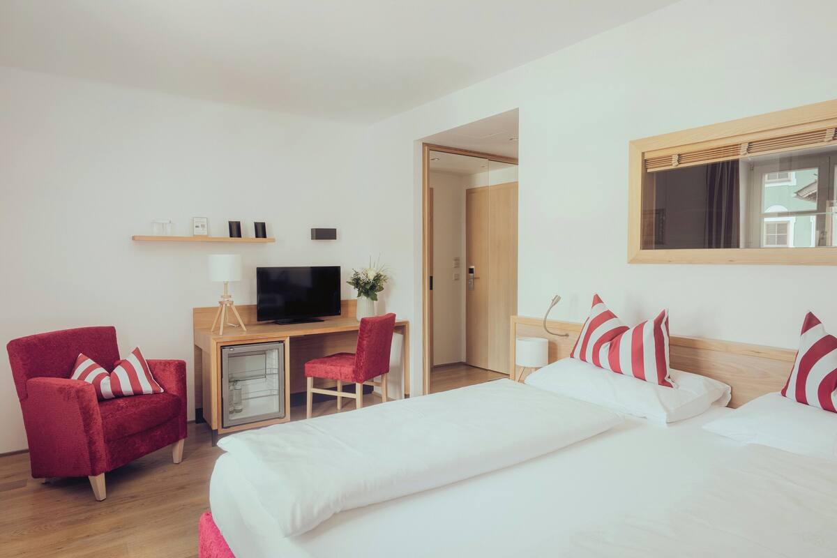 Habitación de hotel con dos camas, un escritorio con televisor, una silla y un armario pequeño.