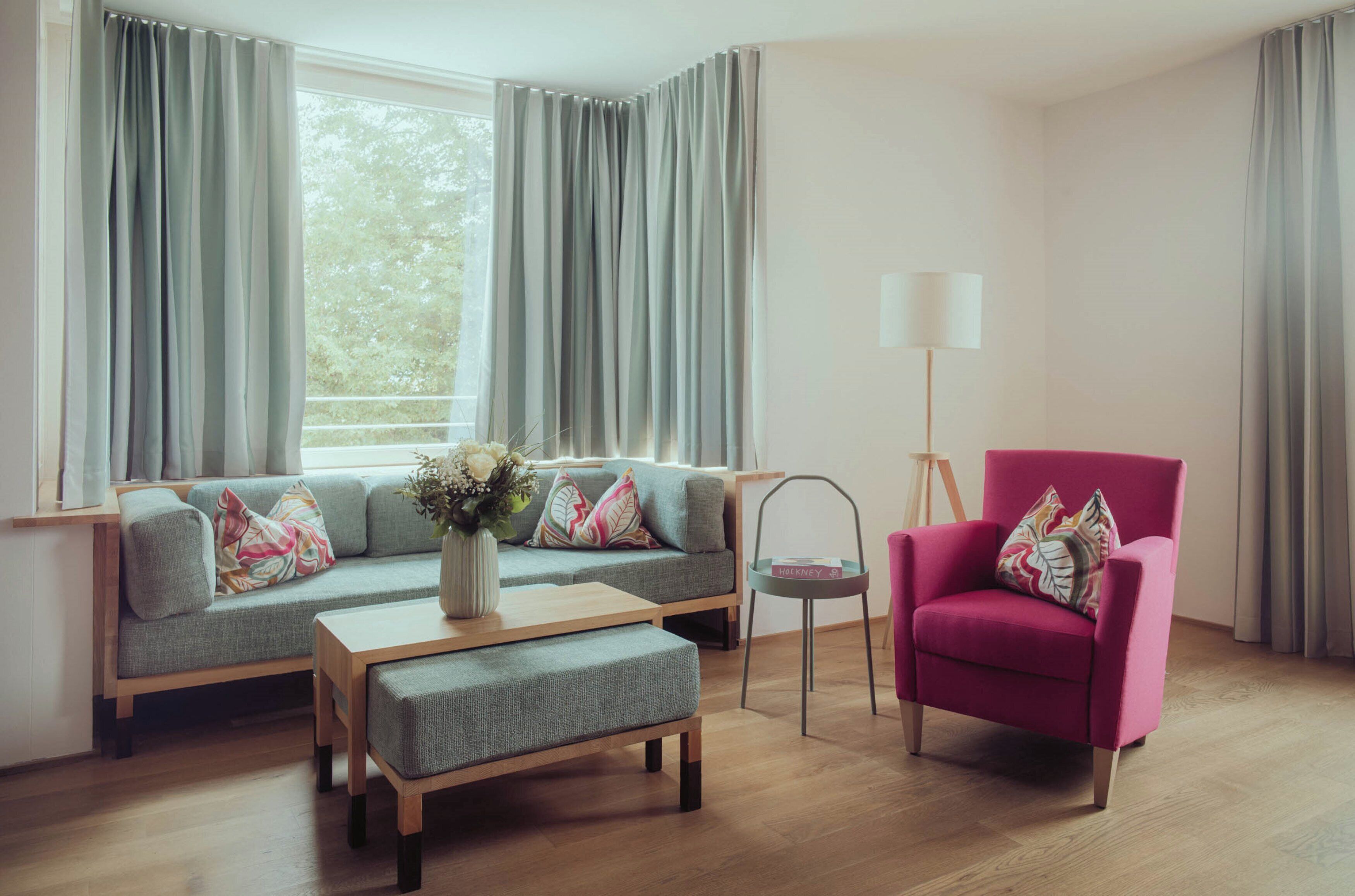 Un salon moderne avec un canapé gris, un fauteuil rose, une table basse en bois et un lampadaire.