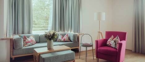 Un salon moderne avec un canapé gris, un fauteuil rose, une table basse en bois et un lampadaire.
