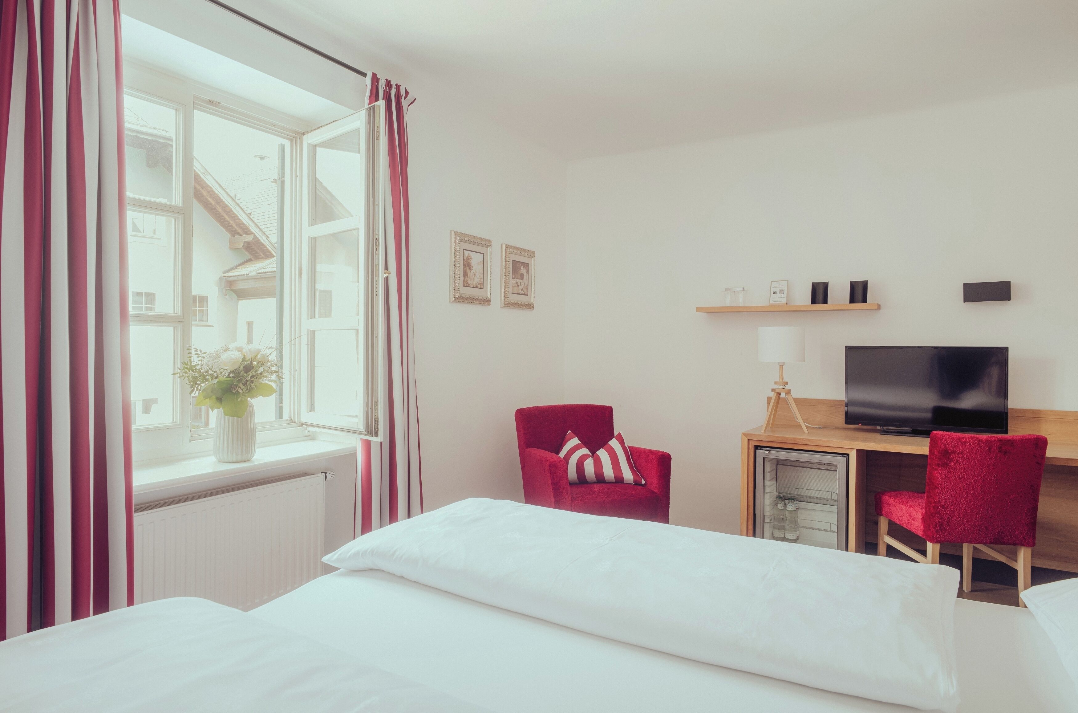 A hotel room with a bed, a desk with a television, a chair, and a window with curtains.