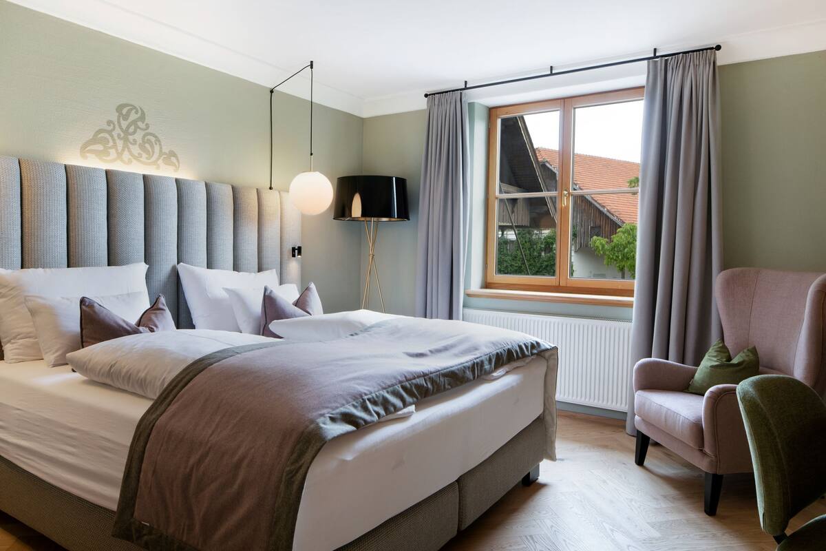 Un dormitorio ordenado con una cama grande, una silla, un televisor y una ventana con cortinas.