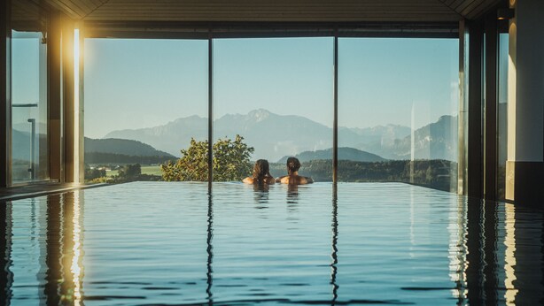 A couple in a large indoor swimming pool with a mountain view.