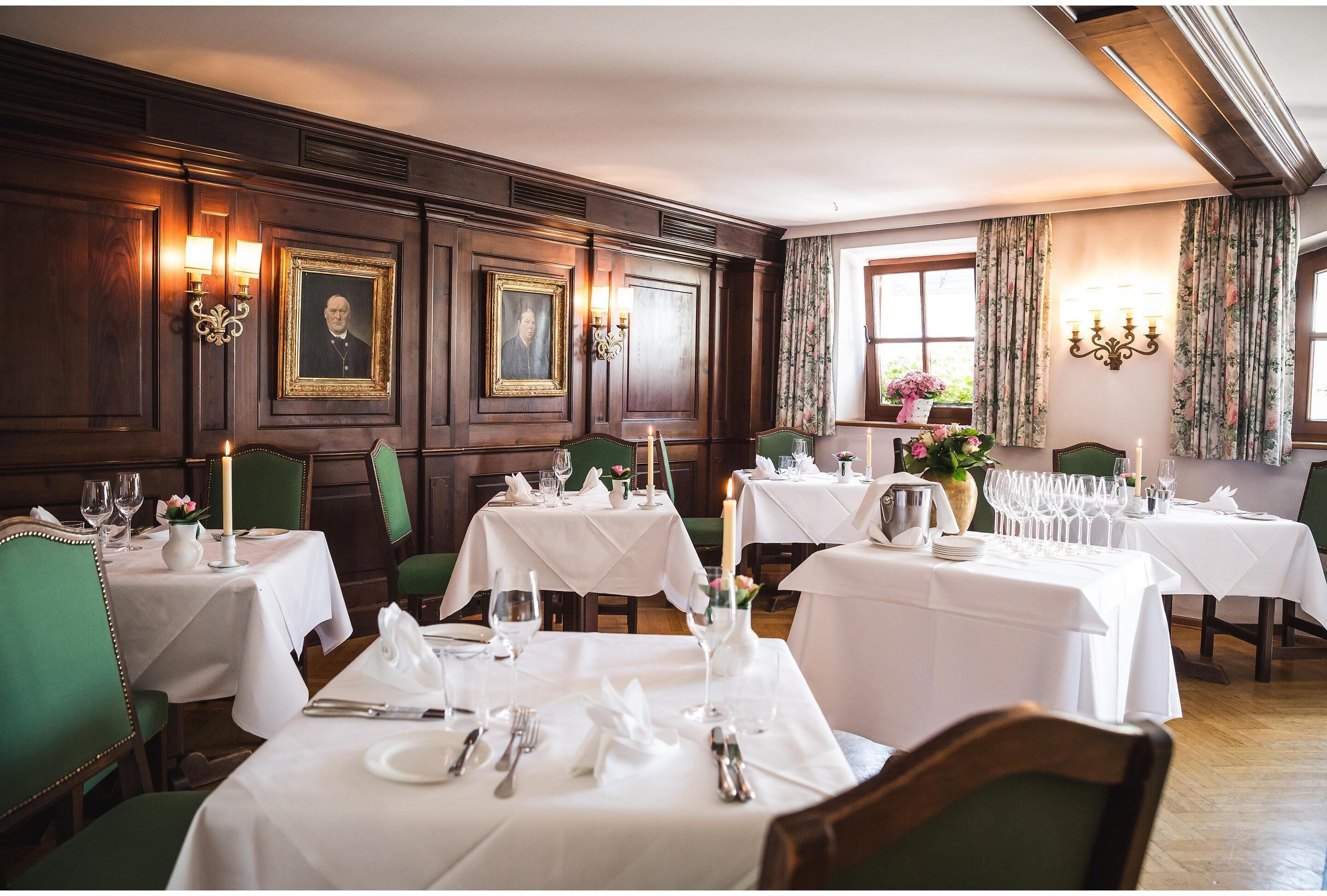 A dining area with tables set for a meal, featuring green chairs, white tablecloths, and candle centerpieces.