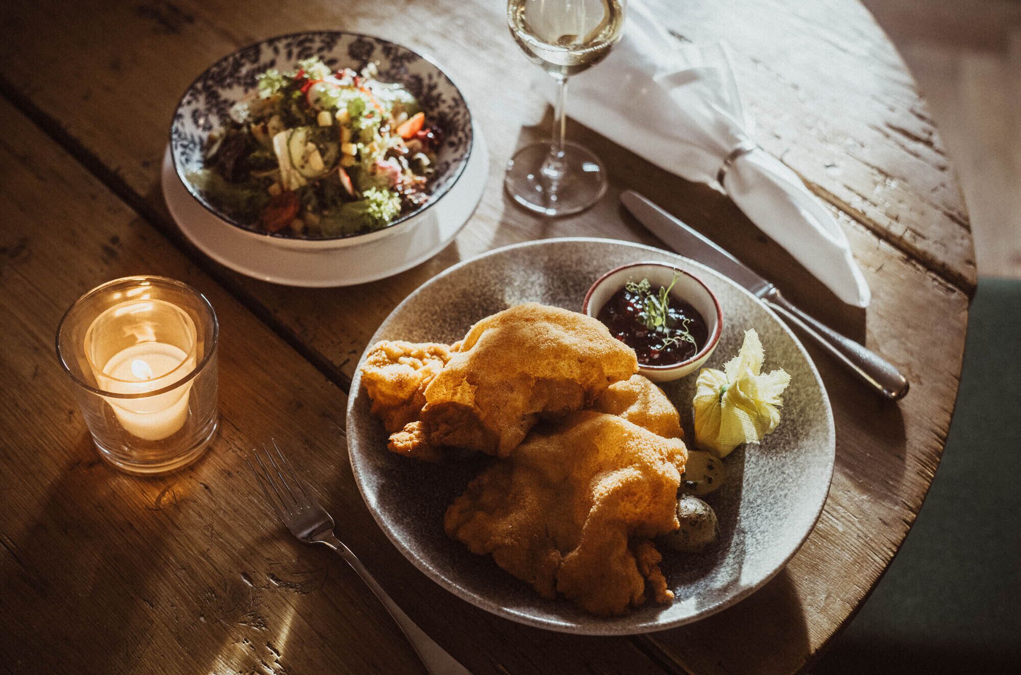 A plate of fried chicken, a bowl of salad, and a glass of wine on a wooden table.