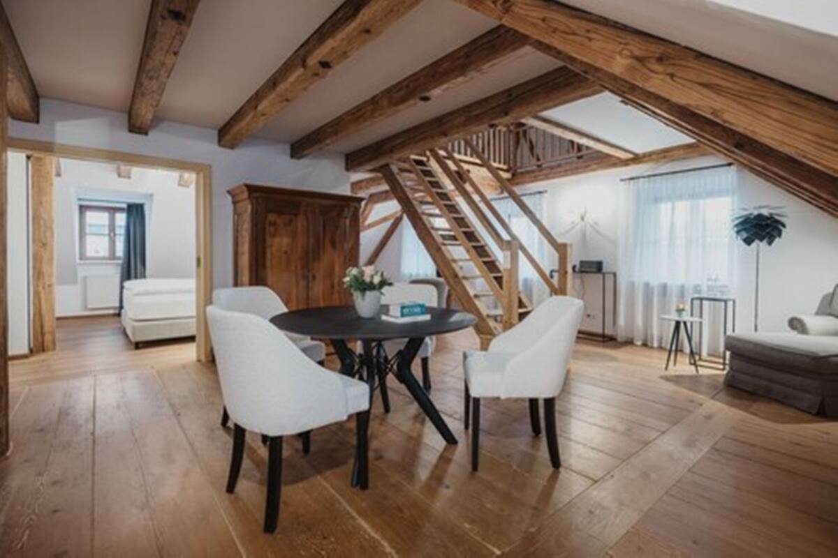 Una habitación estilo loft con vigas de madera a la vista, una escalera, una mesa de comedor con sillas y un sofá.