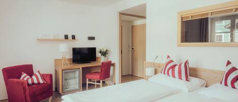 Habitación de hotel con dos camas, un escritorio con televisor, un sillón rojo y un armario pequeño.