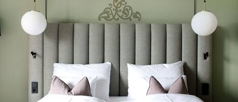 Una cama bien hecha con ropa de cama blanca y rosa, un cabecero tapizado a rayas y dos lámparas colgantes.