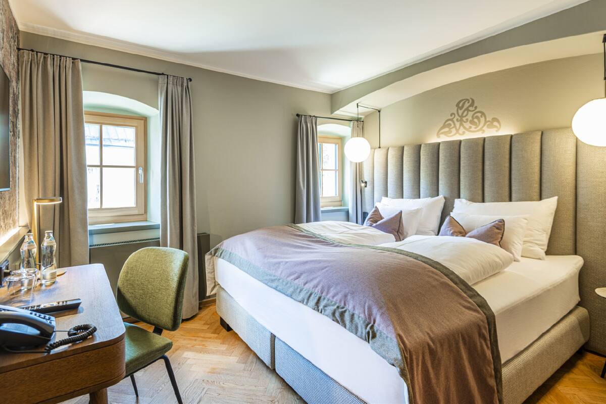 Una habitación de hotel con una cama grande, un escritorio con teléfono y dos ventanas con cortinas.