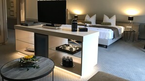 Una habitación de hotel moderna con una cama grande, un escritorio con televisión de pantalla plana, una cafetera y una mesita redonda con un arreglo floral.