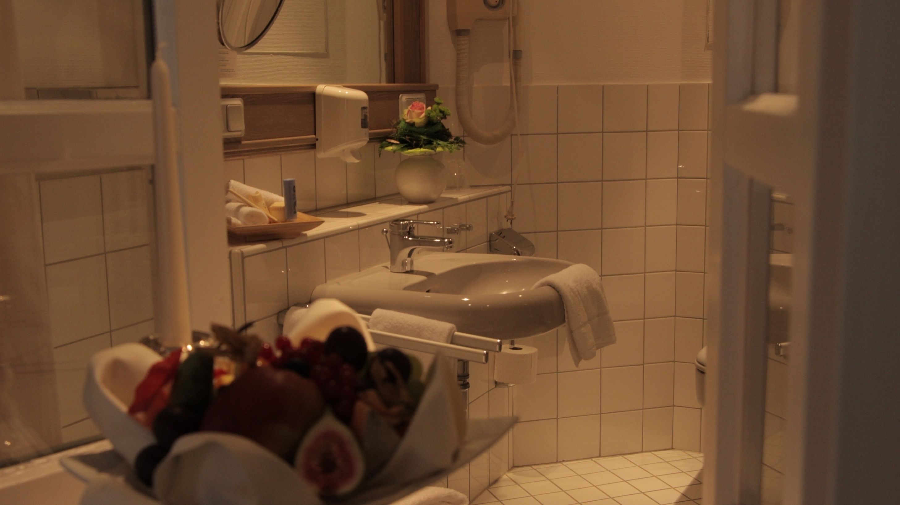 A bathroom with a sink, mirror, and towel rack. There is a bowl with a flower arrangement on the counter.