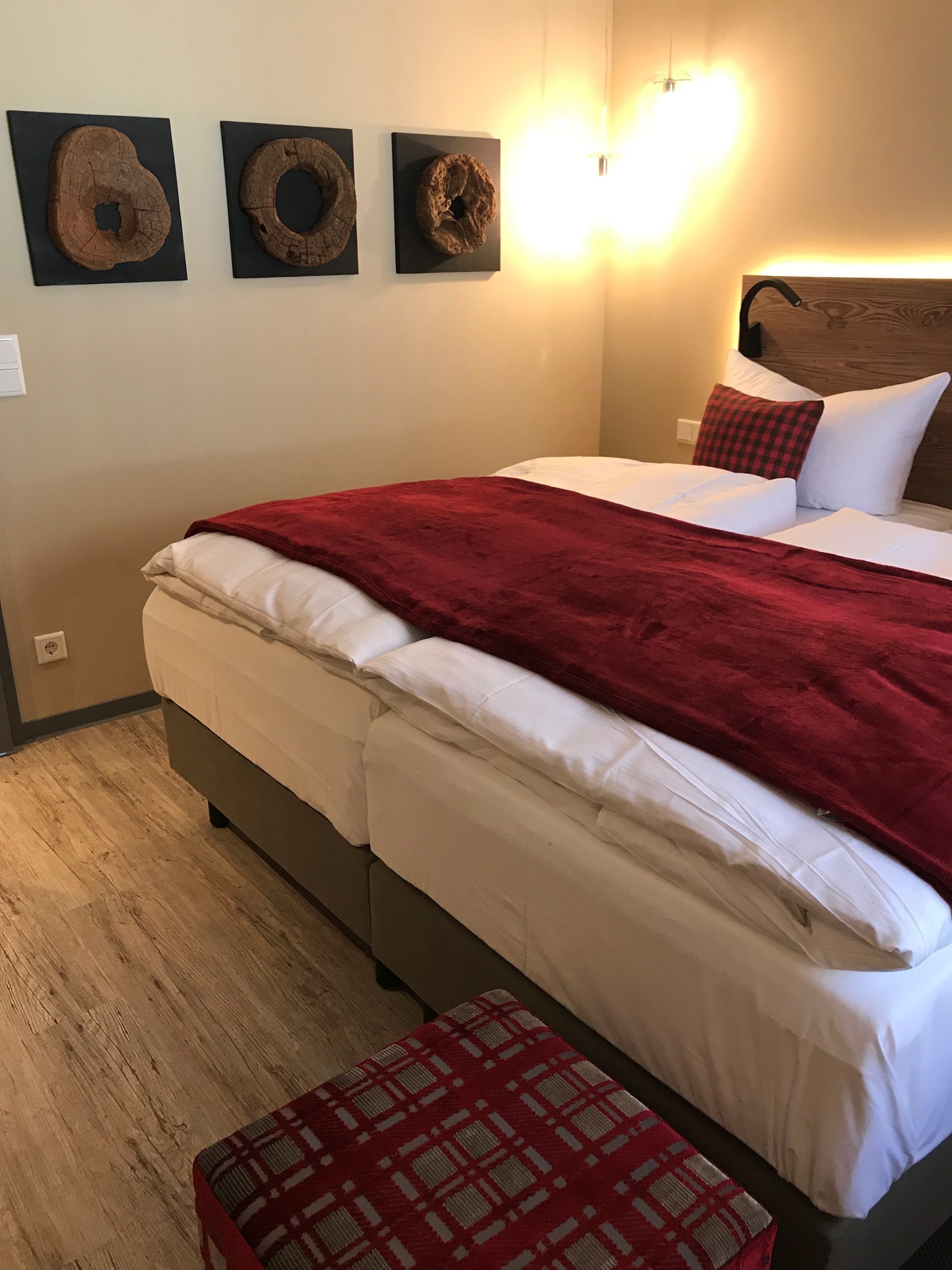Un dormitorio con cama, una colcha roja, cabecera de madera y tres piezas de arte de madera colgadas en la pared.
