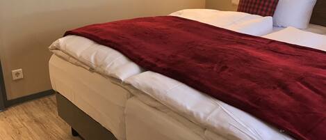 Un dormitorio con cama, una colcha roja, cabecera de madera y tres piezas de arte de madera colgadas en la pared.
