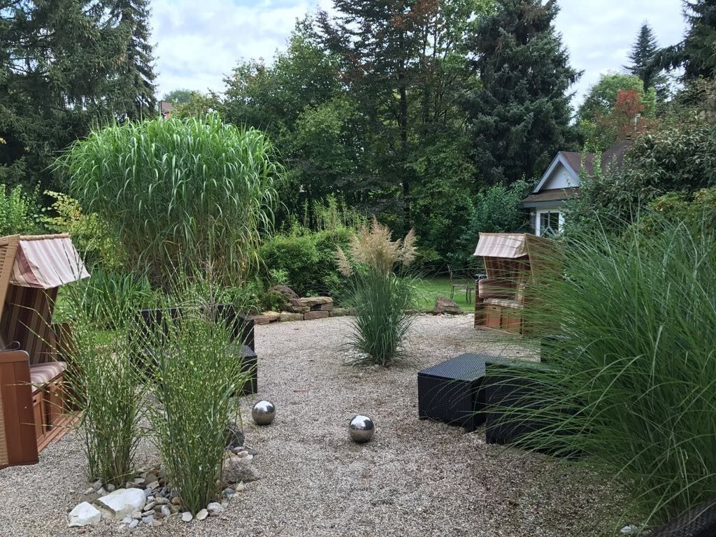 Jardí amb camí de grava, construccions de fusta i diferents plantes.