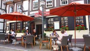 Un café al aire libre con mobiliario de mimbre y sombrillas rojas, situado frente a un edificio con un cartel que dice "RESTAURANT".