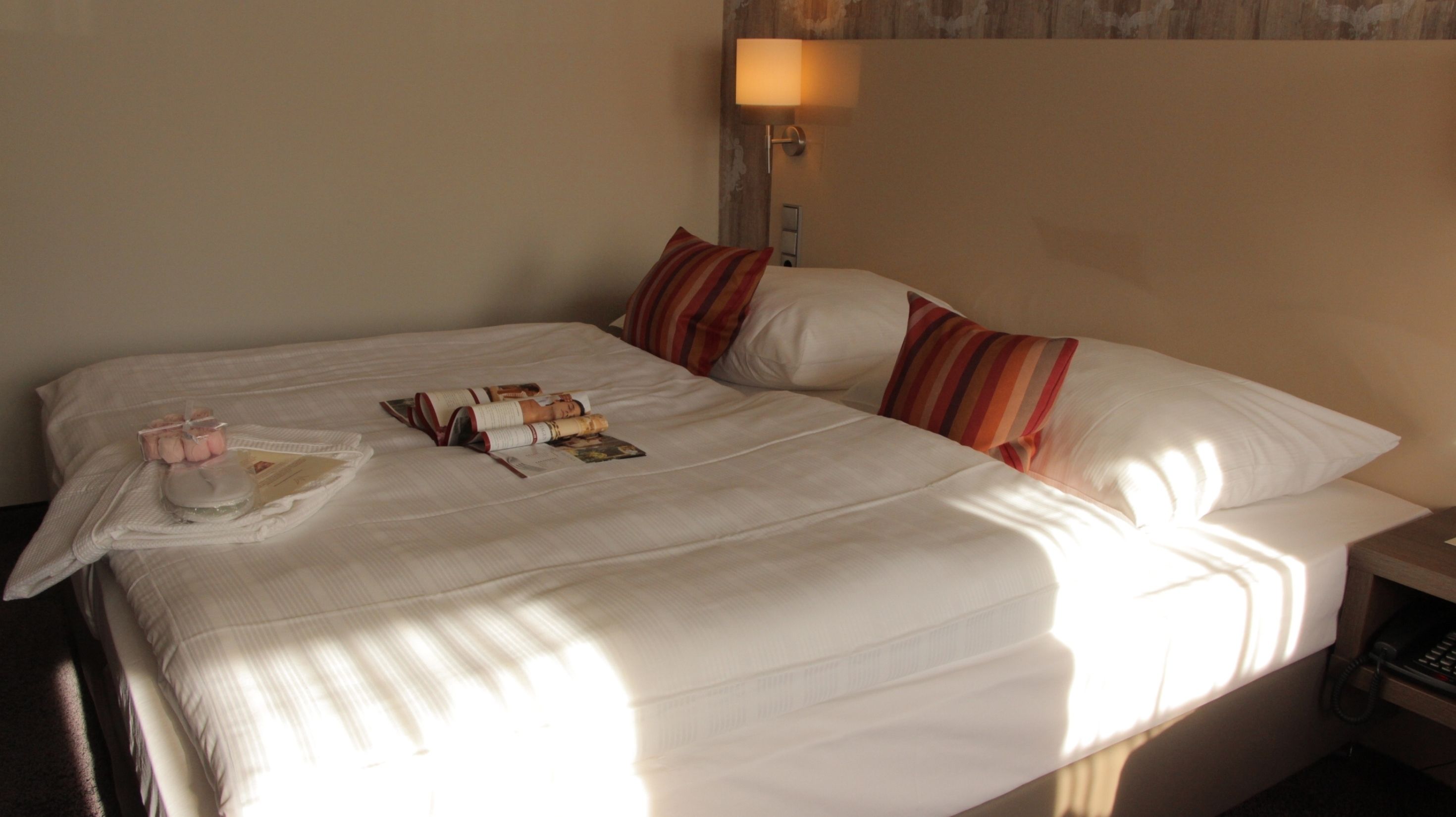 A neatly made bed with a white comforter, striped pillows, and a bedside lamp.