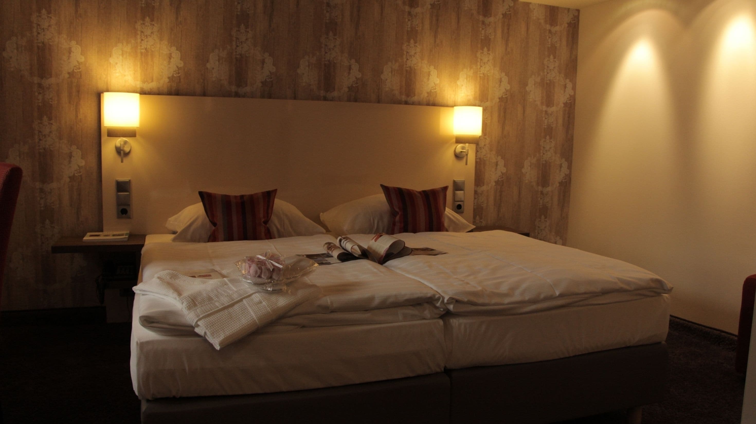Een hotelkamer met een groot bed, twee bedlampjes en een houten hoofdeinde.