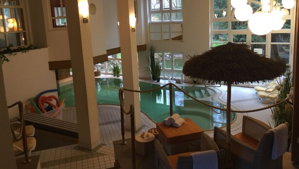 Zona de piscina con barrera de cuerda, sillas de descanso y sombrilla de paja.