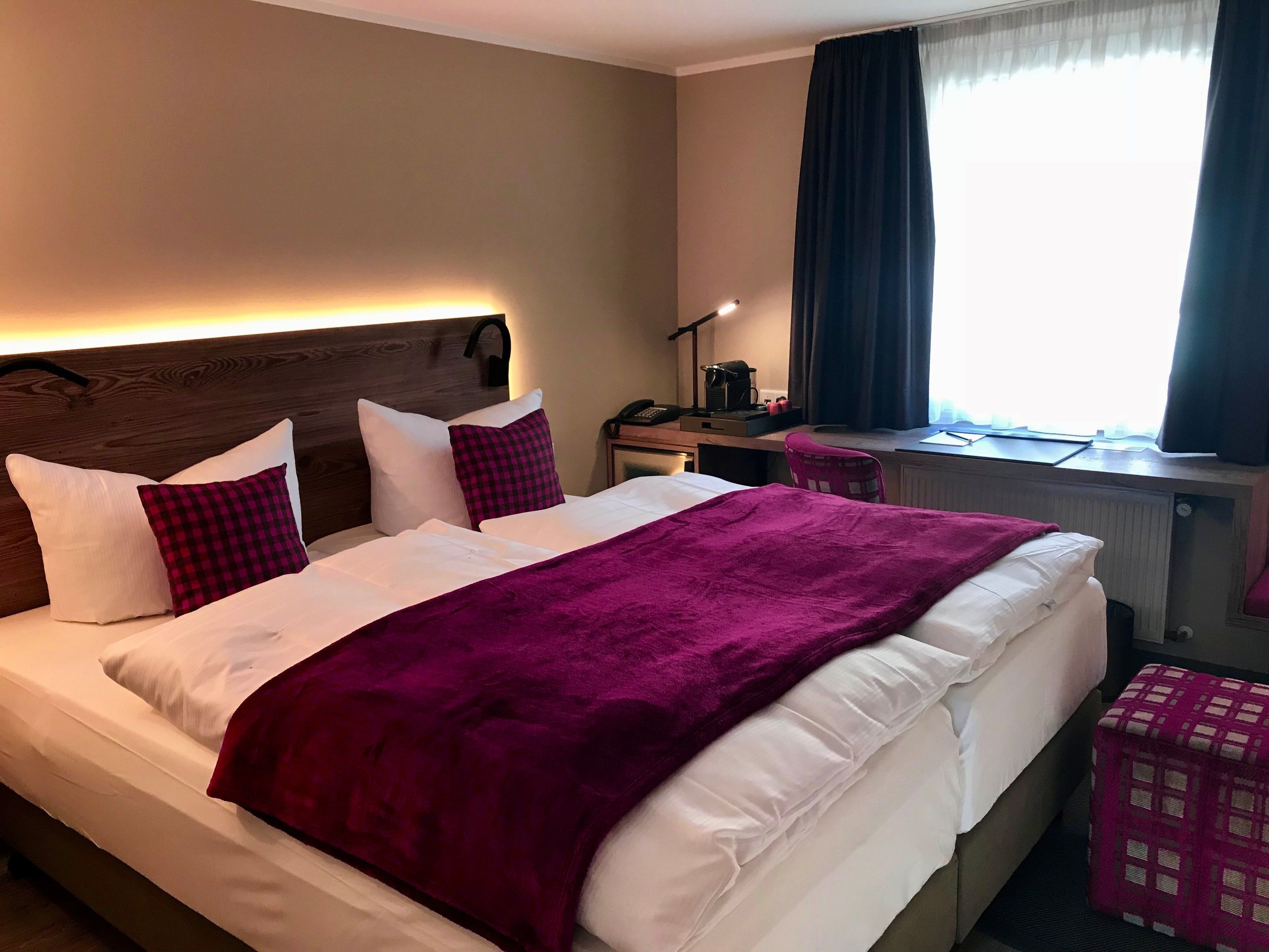 Une chambre d’hôtel avec un lit, un bureau, une chaise et une fenêtre avec des rideaux.