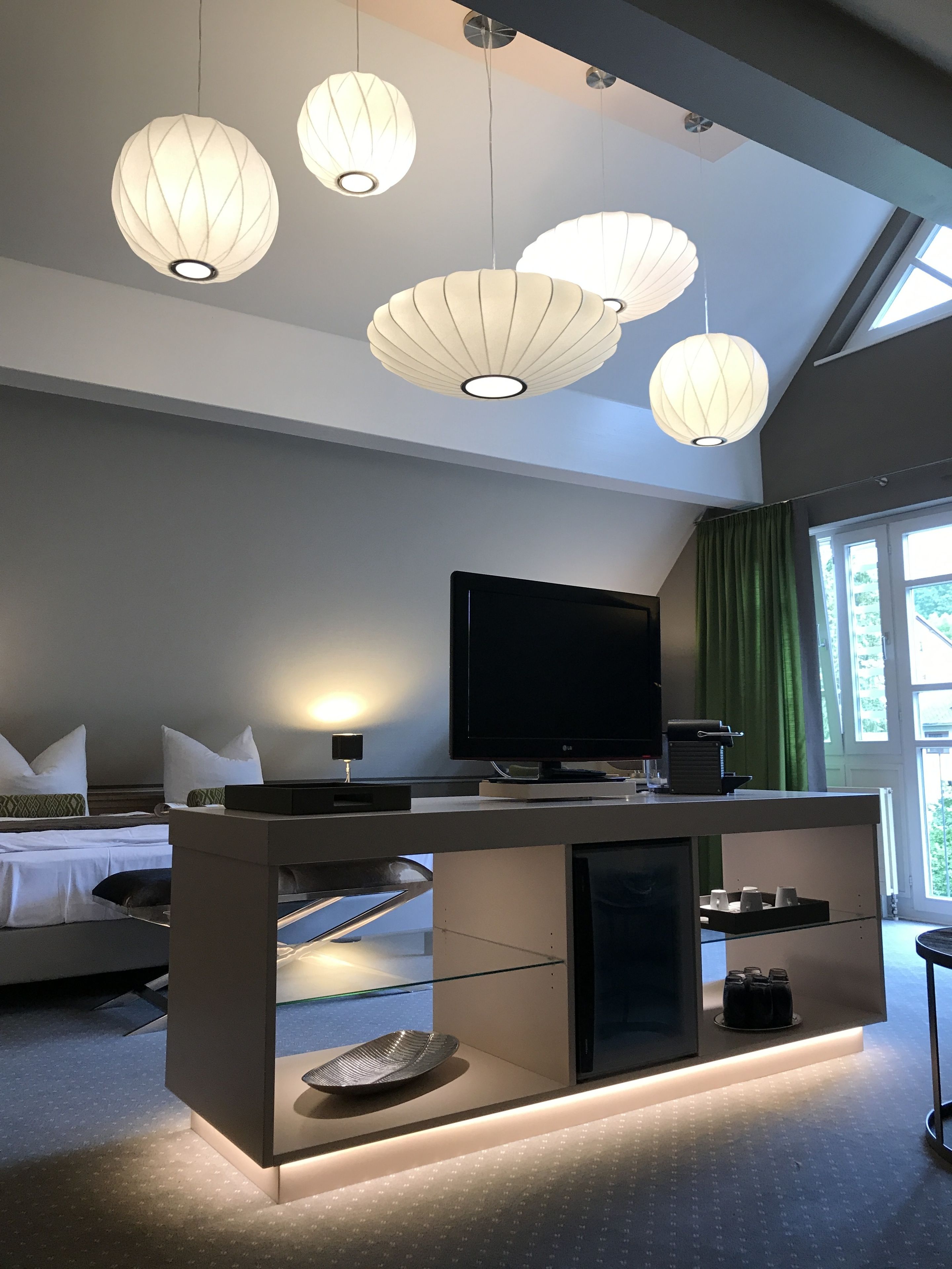 Una moderna camera d'albergo con televisione a schermo piatto, una scrivania con piano in vetro e un'ampia finestra con tende.