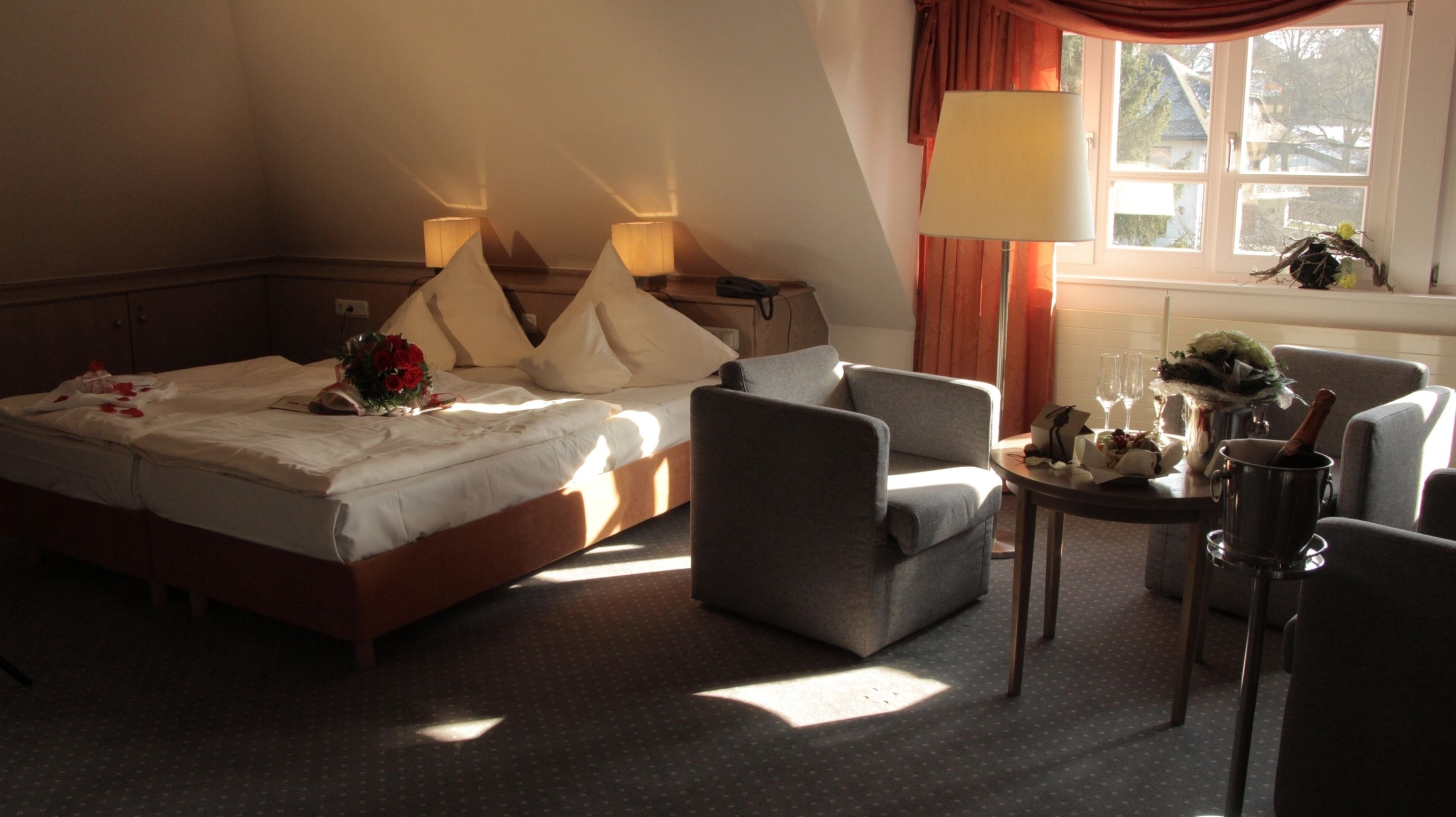 Ein Hotelzimmer mit einem Bett, zwei Sesseln, einem kleinen Tisch mit Lampe und einem fenster mit Vorhängen.