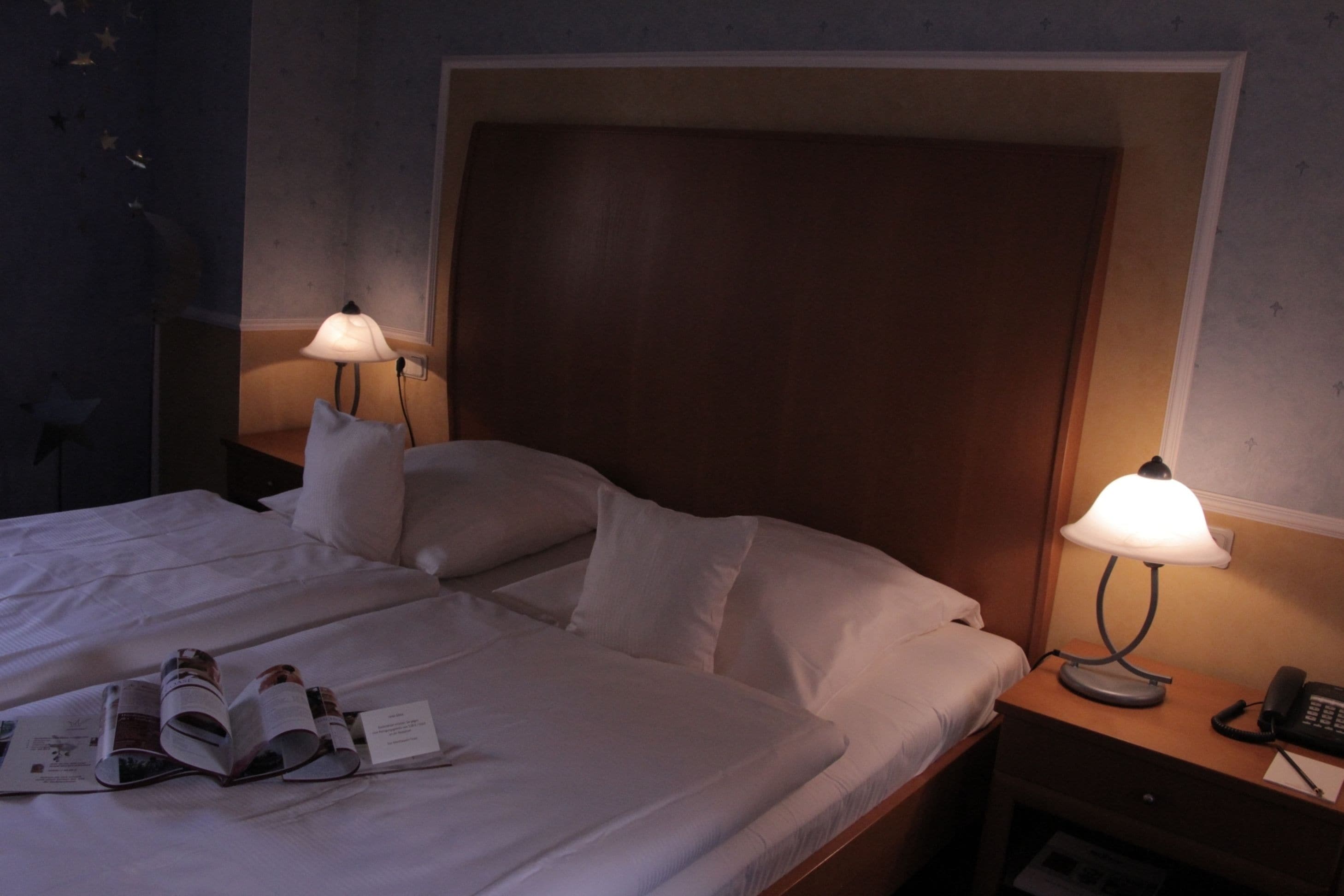 Ein Hotelzimmer mit einem großen Bett, zwei Nachttischlampen, einem Nachttisch mit Telefon und einer Wand mit Sternenverzierungen.
