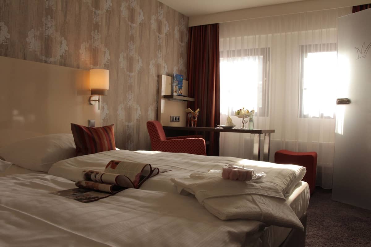 Habitación de hotel con una cama grande, un escritorio, una silla, una lámpara y una ventana con cortinas.