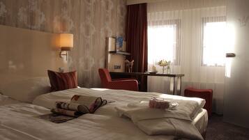 Habitación de hotel con una cama grande, un escritorio, una silla, una lámpara y una ventana con cortinas.