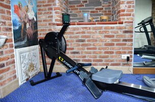 A stationary bike with a digital display, a brick wall, and a painting.
