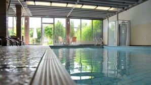 Una piscina interior con agua cristalina, suelo de baldosas y vistas al exterior con zonas verdes.