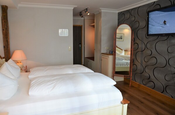 A hotel room with a large bed, a bedside lamp, a mirror, and a television on the wall. - Ringhotel Alpenhof (Augsburg)