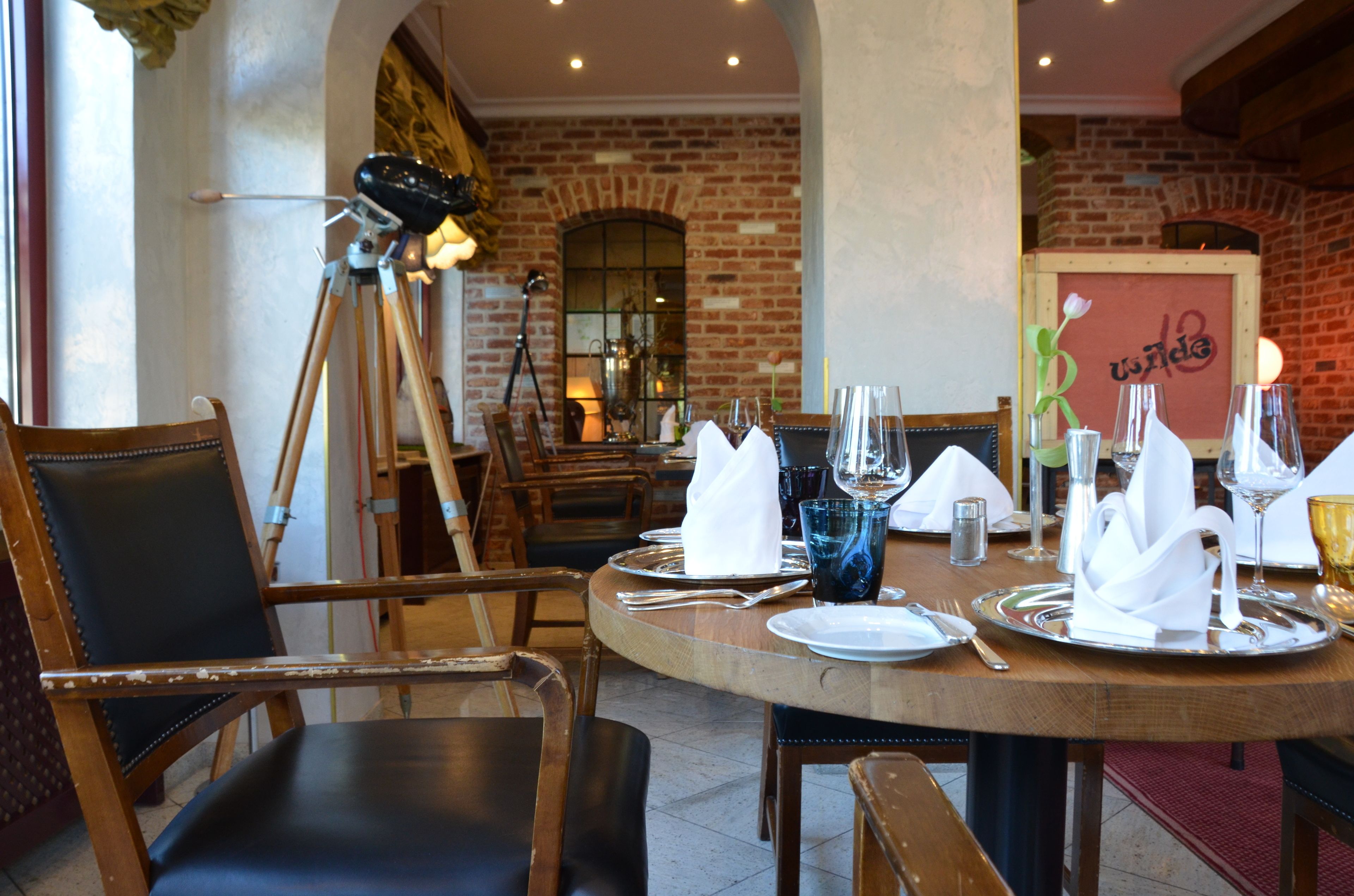A restaurant setting with a brick wall, wooden chairs, and a round table set for dining.