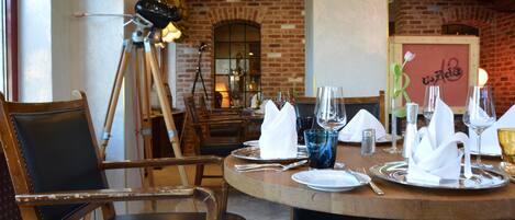 Un ambiente de restaurante con pared de ladrillo, sillas de madera y una mesa redonda dispuesta para comer.