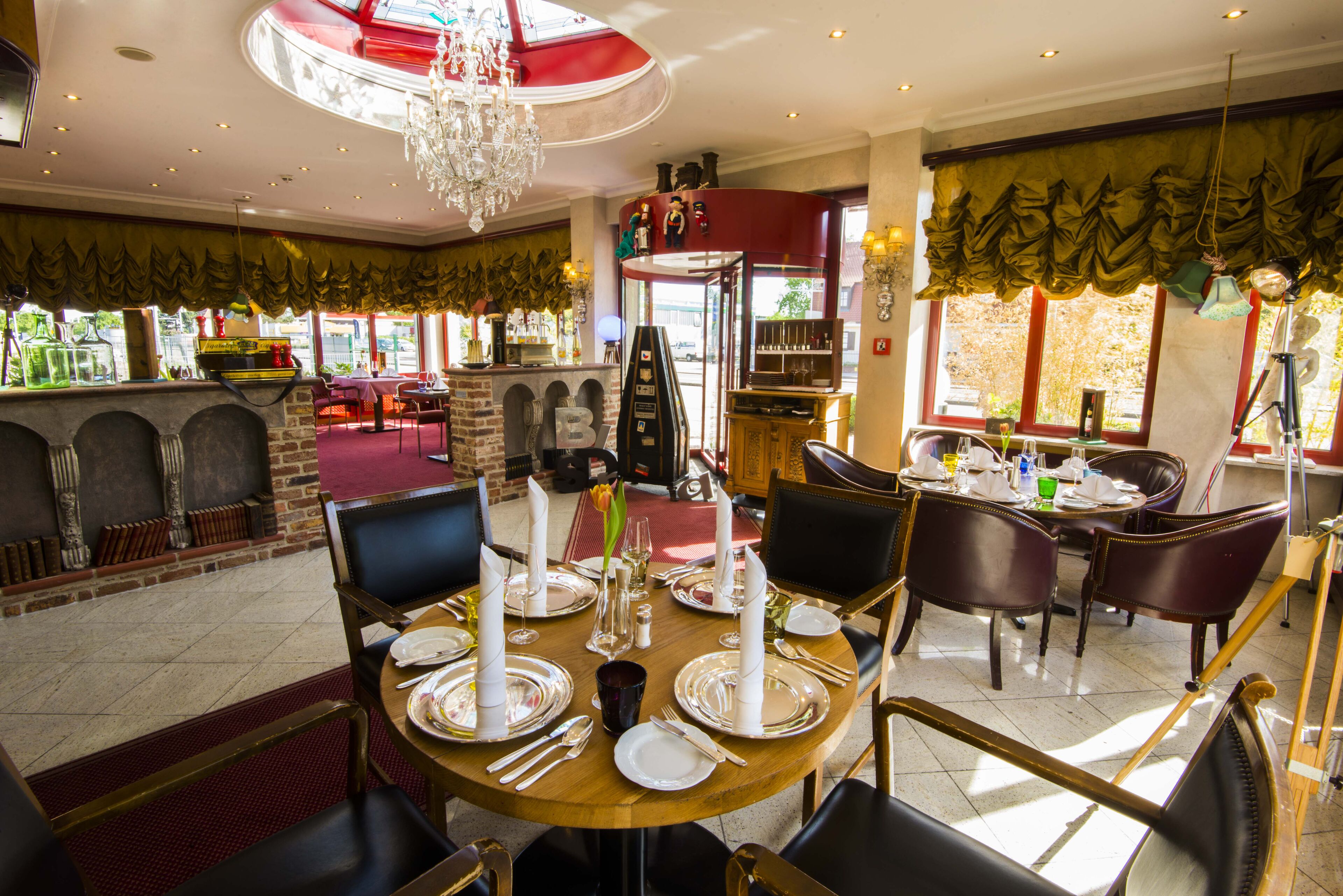 A restaurant with a round table set for four, surrounded by chairs. There is a chandelier above the table, and the room has a red and green color scheme.