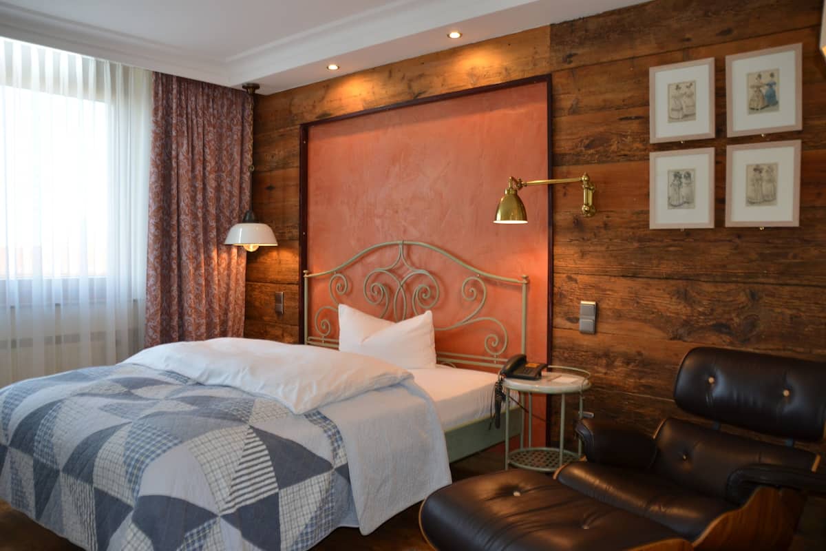 Een hotelkamer met een bed, een leren fauteuil, een nachtkastje met een lamp en kunst aan de muur.