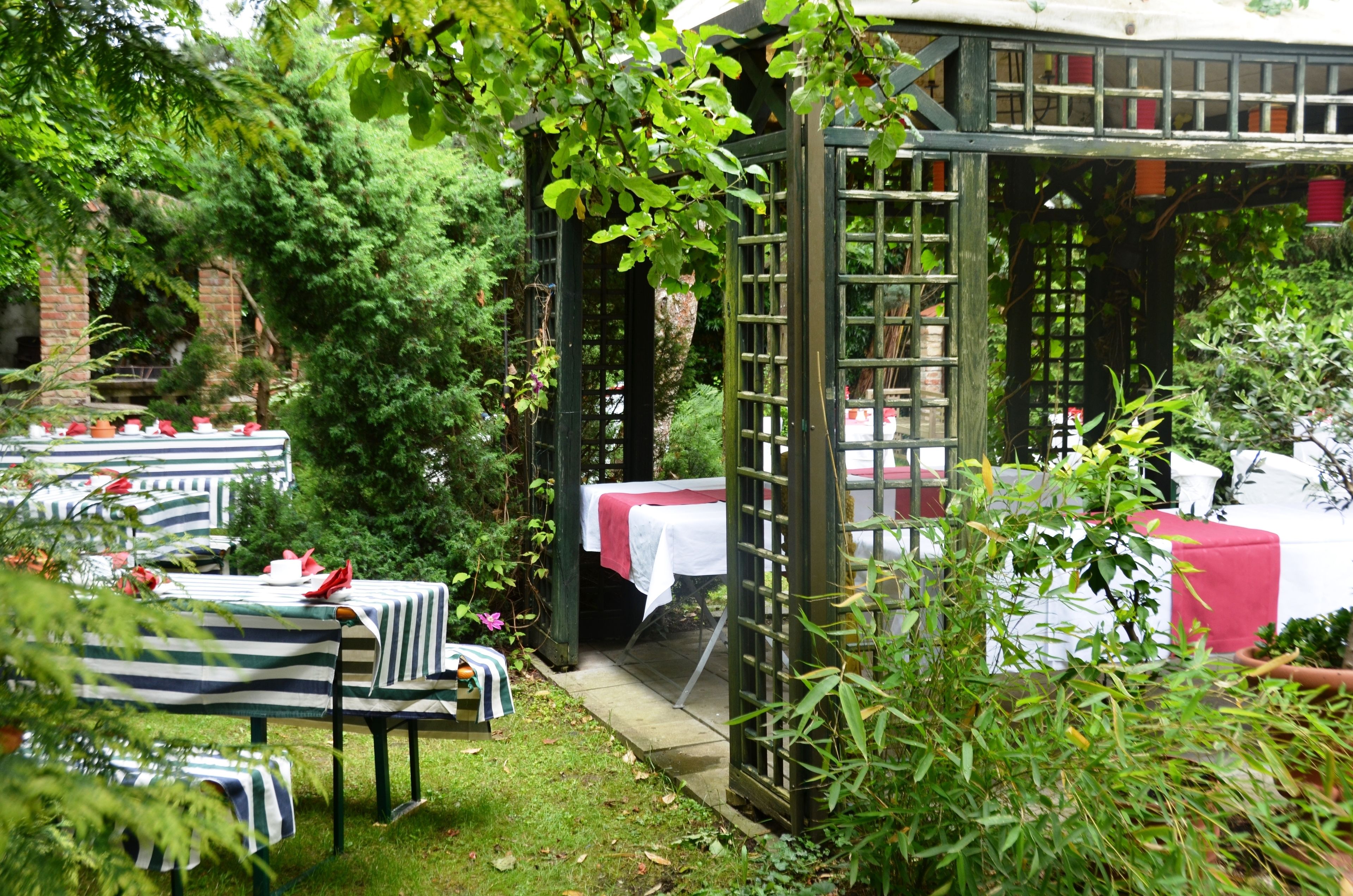 An outdoor garden with tables set up for dining, surrounded by greenery and a wooden pergola.