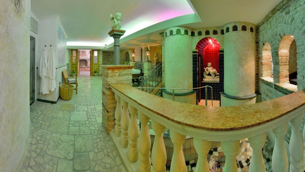 Un vestíbulo con suelo de piedra, un mostrador de recepción curvo de mármol, una escalera y un arco iluminado en rojo.