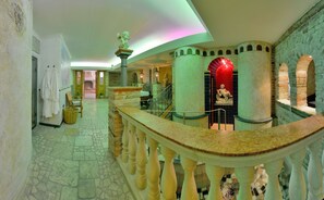 Un vestíbulo con suelo de piedra, un mostrador de recepción curvo de mármol, una escalera y un arco iluminado en rojo.