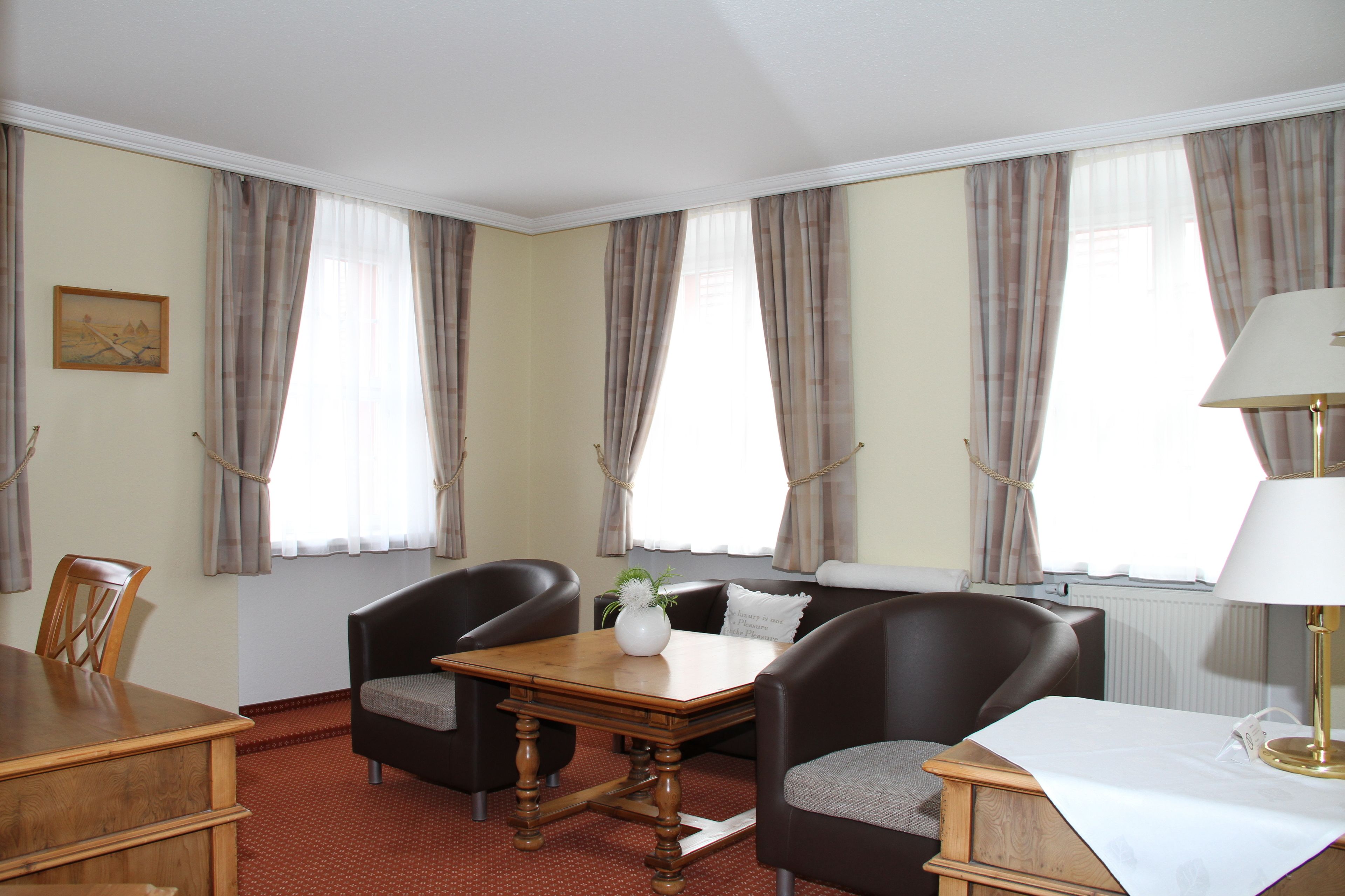 A hotel room with a dining table, two armchairs, a sofa, and a lamp.