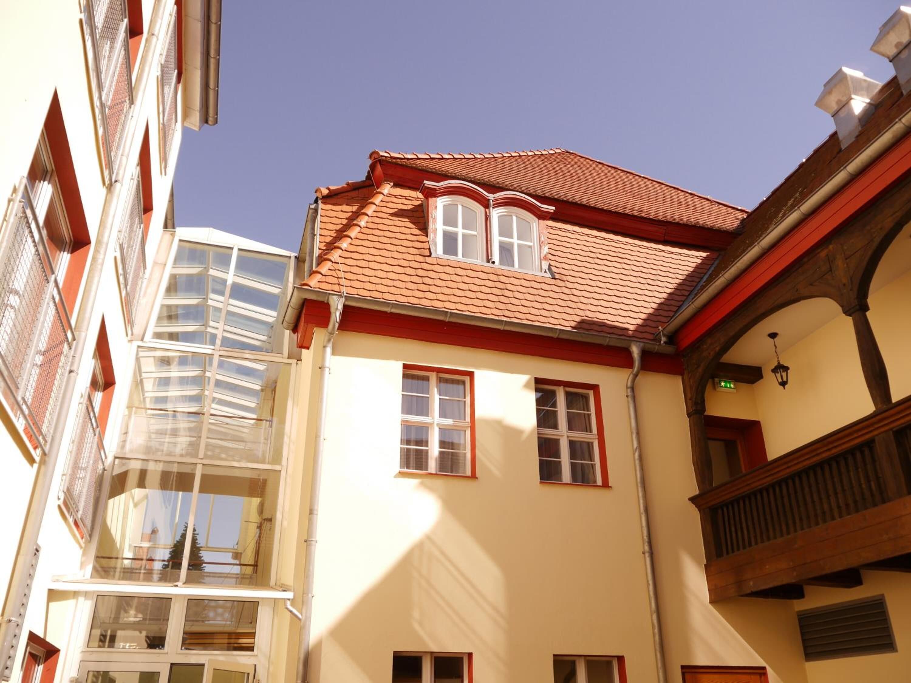 A building with a red-tiled roof, multiple windows, and a balcony with wooden railings.