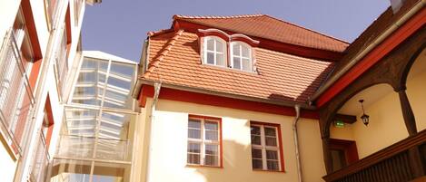 A building with a red-tiled roof, multiple windows, and a balcony with wooden railings.