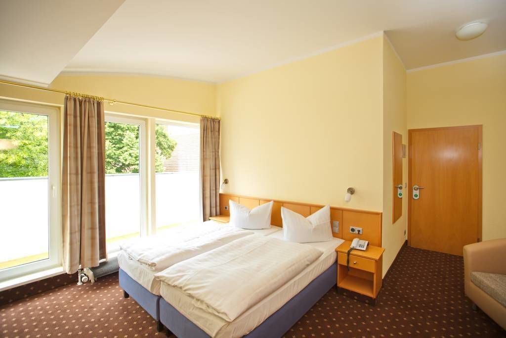 Habitación de hotel con dos camas, una puerta de madera y una ventana con cortinas.