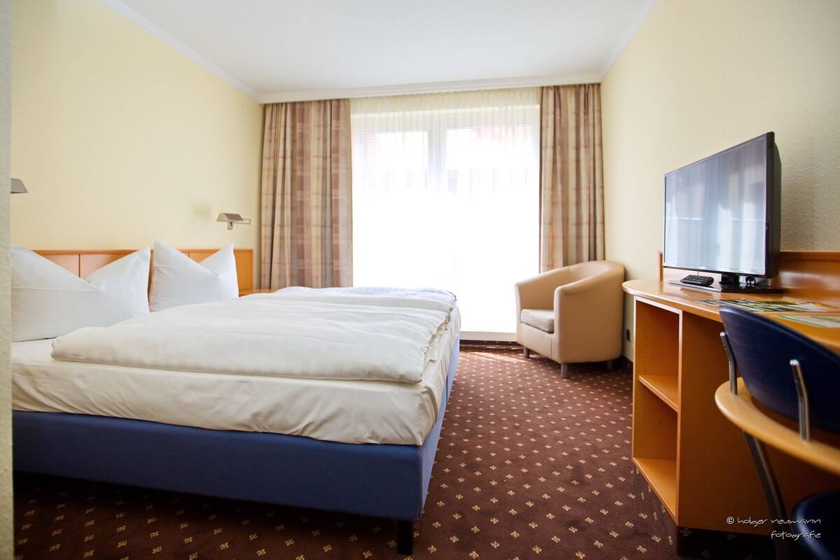 Une chambre d’hôtel avec deux lits, un bureau avec une télévision et une chaise.