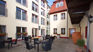 A courtyard with outdoor seating, a large terracotta pot, and a building with multiple windows and balconies. - Bed & Breakfast zum alten Ratskeller (Vetschau/Spreewald)